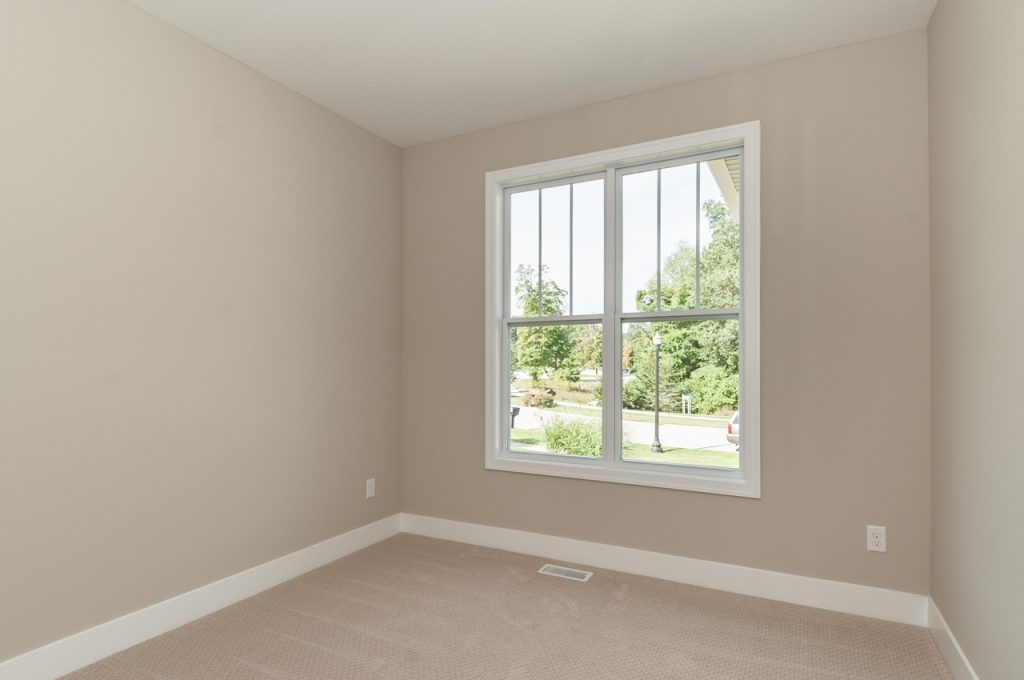 A bedroom with a large window and beige walls.