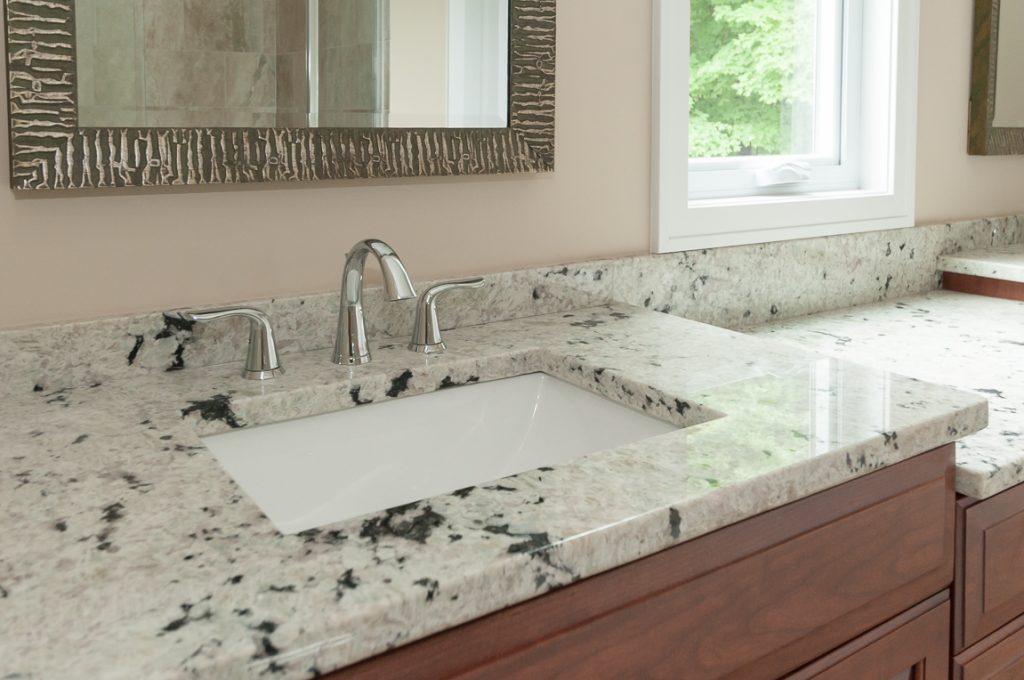 A bathroom with marble counter tops and wooden cabinets.