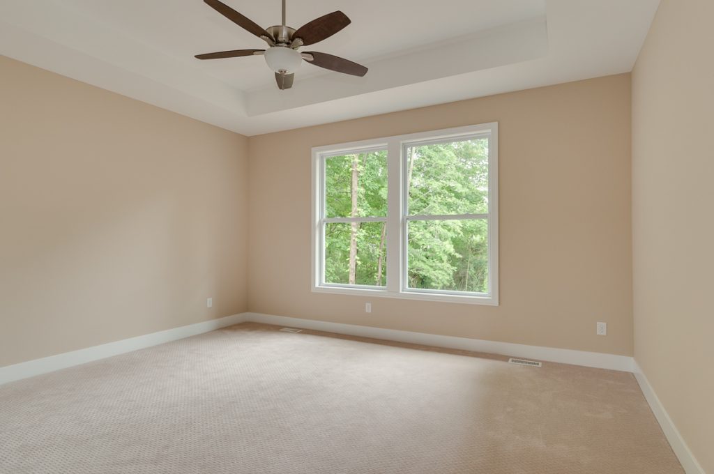 A room with a ceiling fan and two windows.